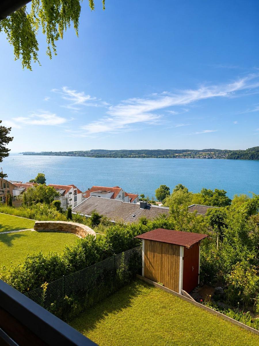 Grüner Garten mit Holzschuppen und Blick auf See und Hügel.