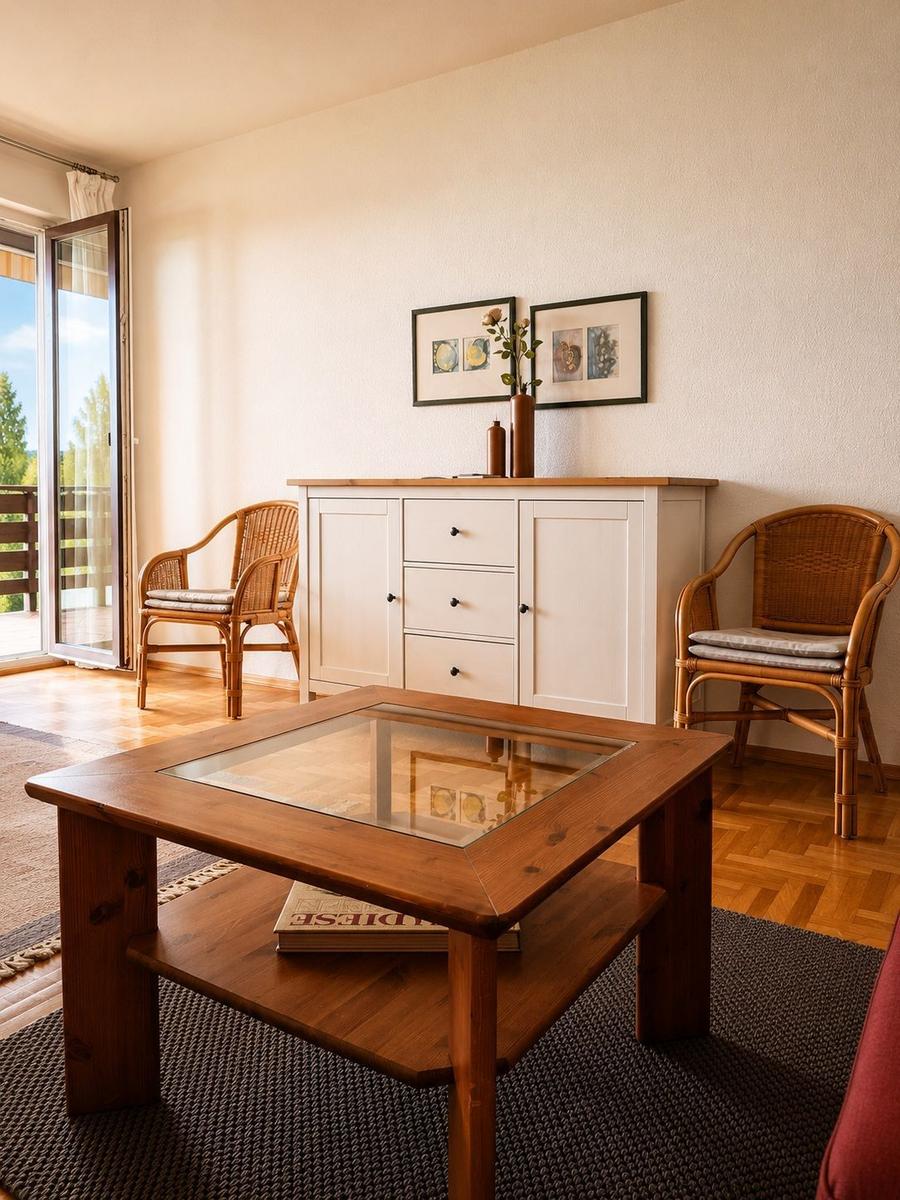 Ein Wohnzimmer mit Holztisch, zwei Rattanstühlen und einem Schrank an der Wand.
