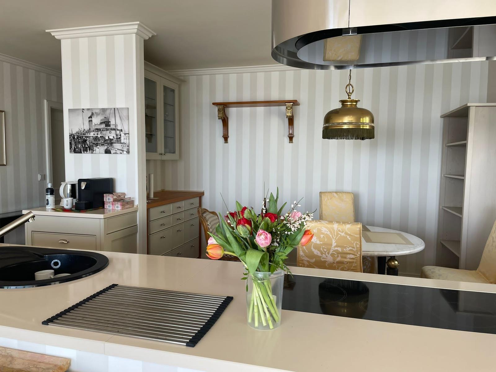 Küche mit Essbereich, Blumen und goldener Deckenleuchte.