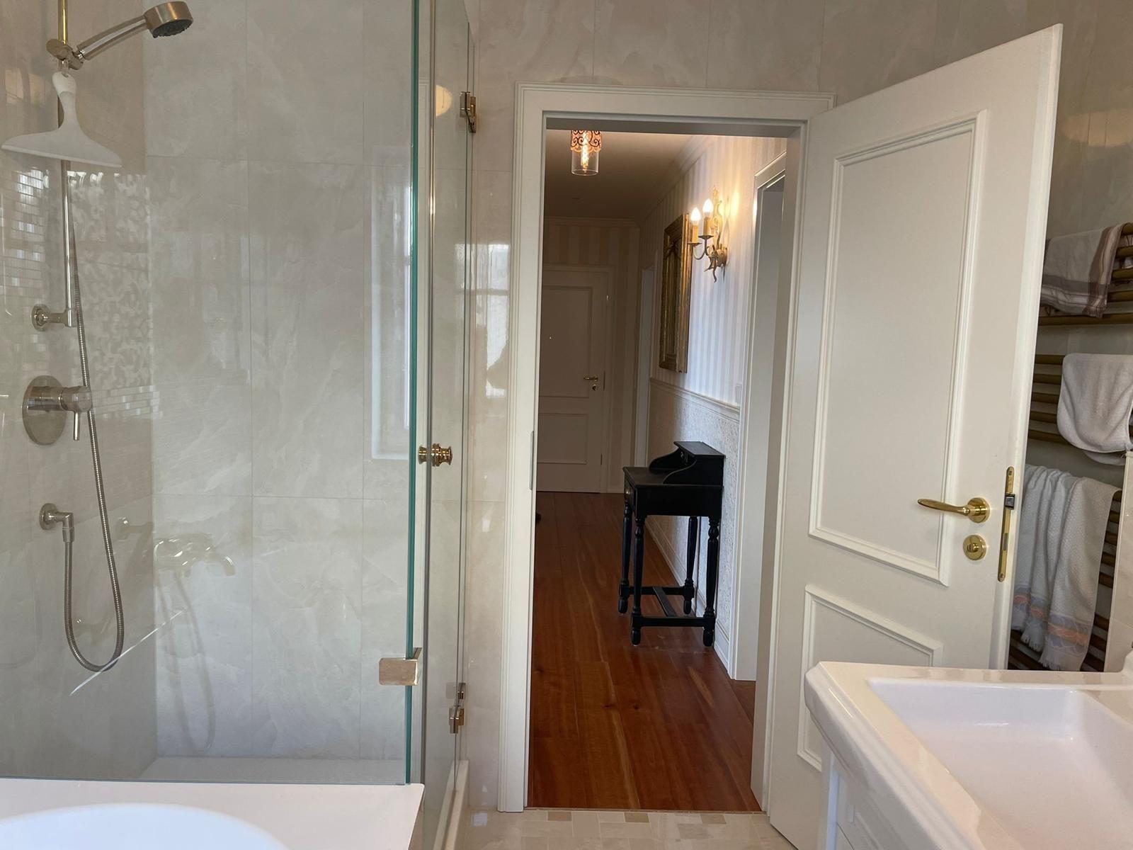 Badezimmer mit Dusche, Waschbecken und Blick in Flur mit Flügel.