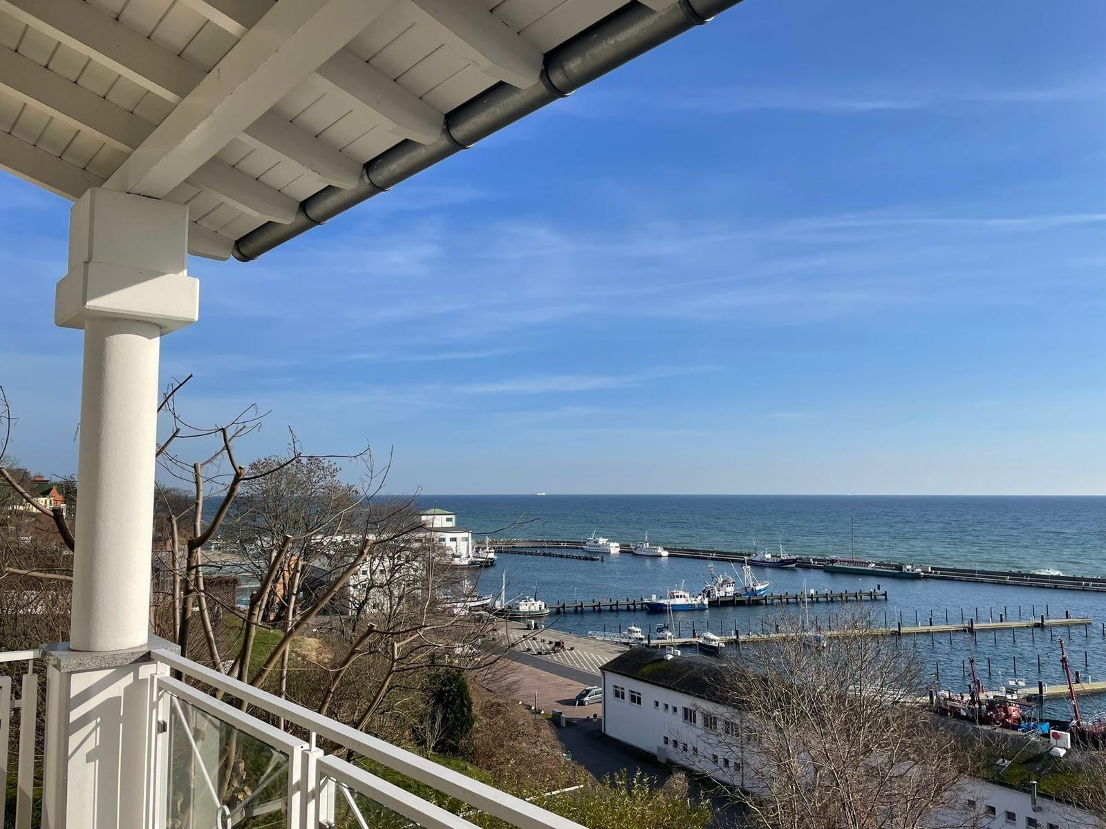 Blick von Balkon auf Hafen mit Booten und Meer unter blauem Himmel