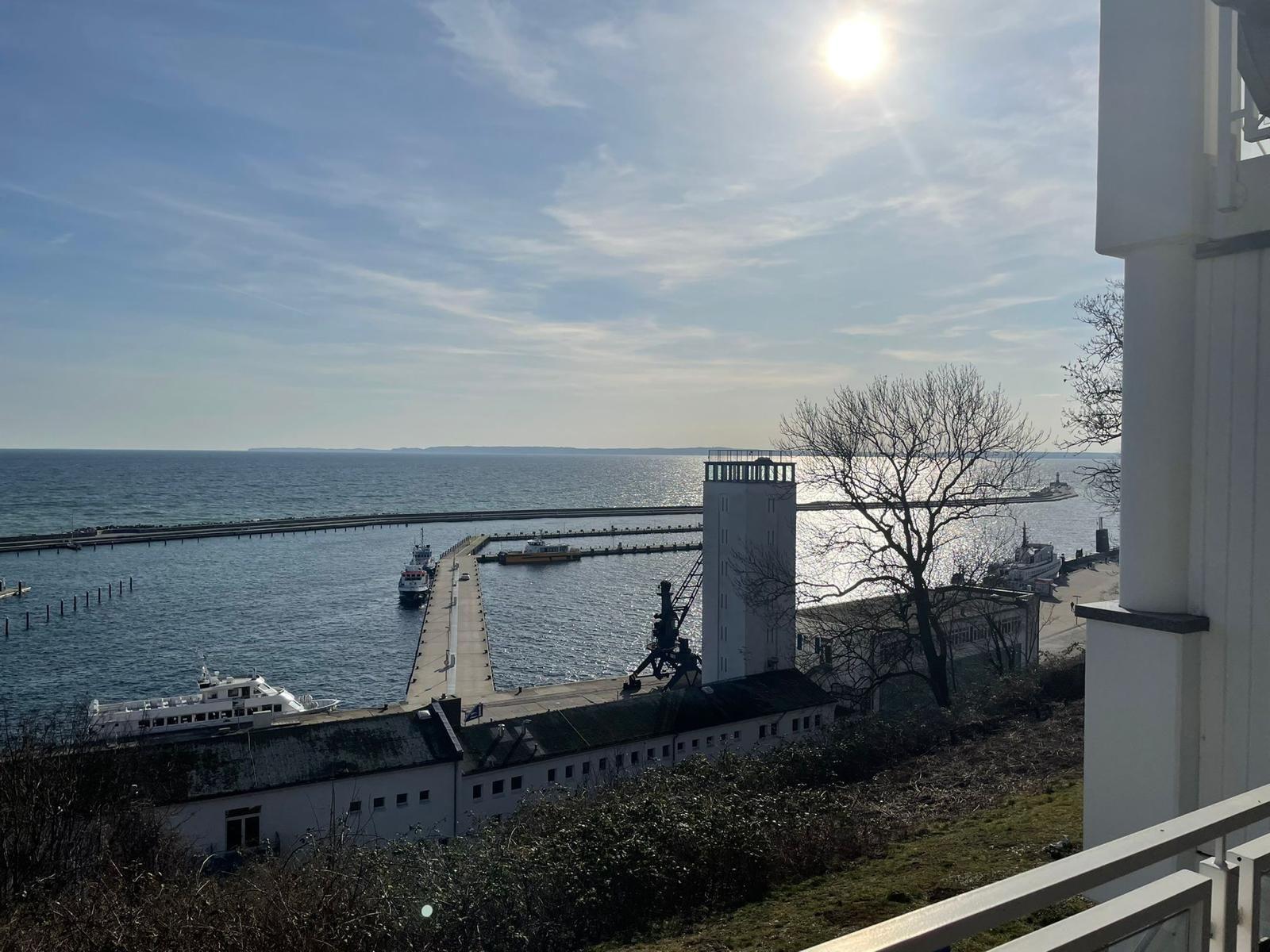 Blick auf Hafen mit Schiffen und Leuchtturm unter blauem Himmel.