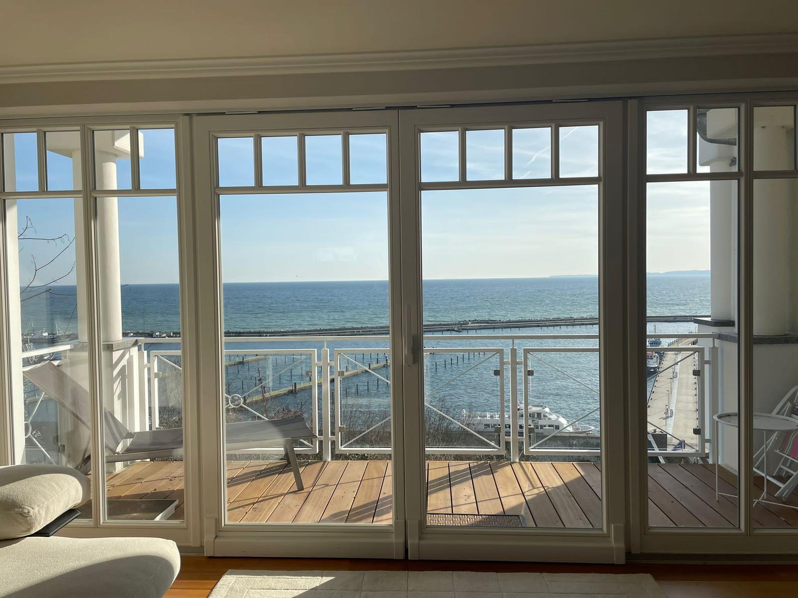 Durch große Fenster blickt man auf einen Hafen mit Booten und das Meer.