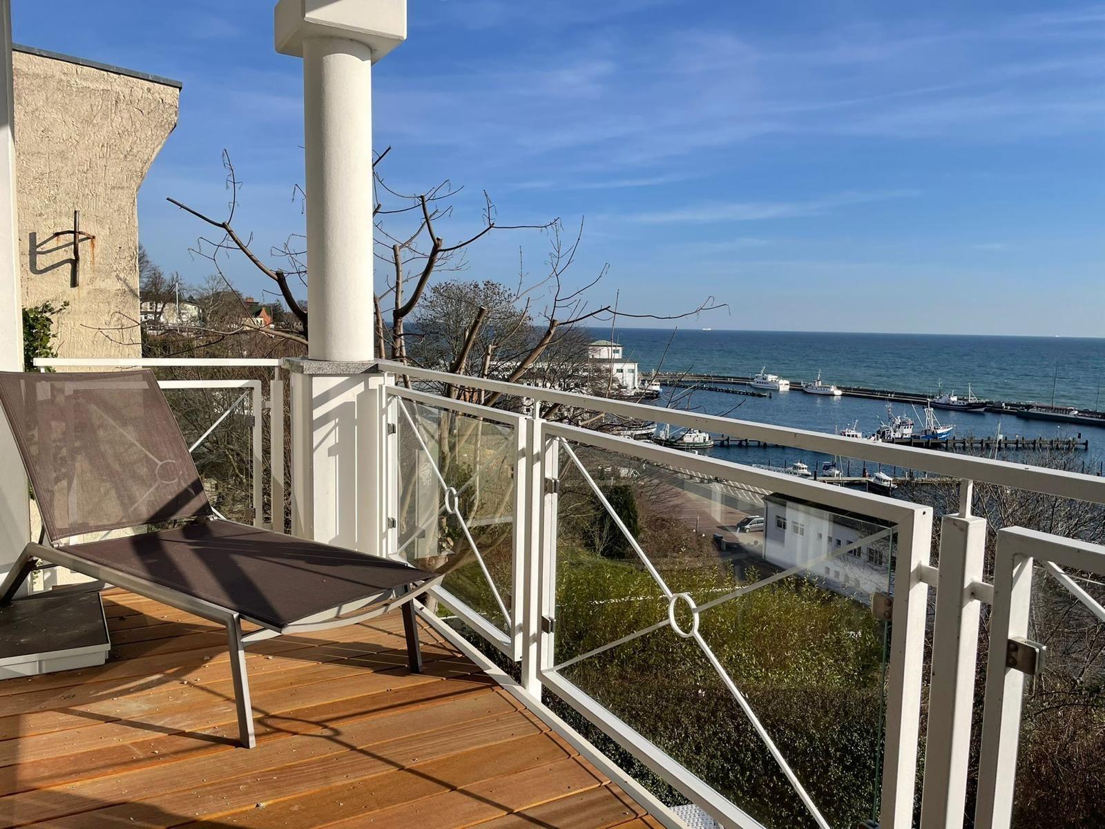 Terrasse mit Liegestuhl und Blick auf Hafen und Meer.