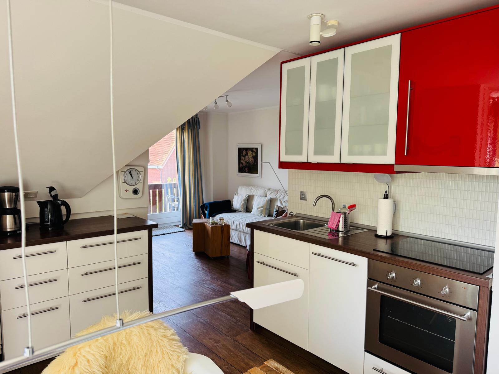 Küche mit roten Schränken und Wohnzimmer mit Sofa und Balkon.