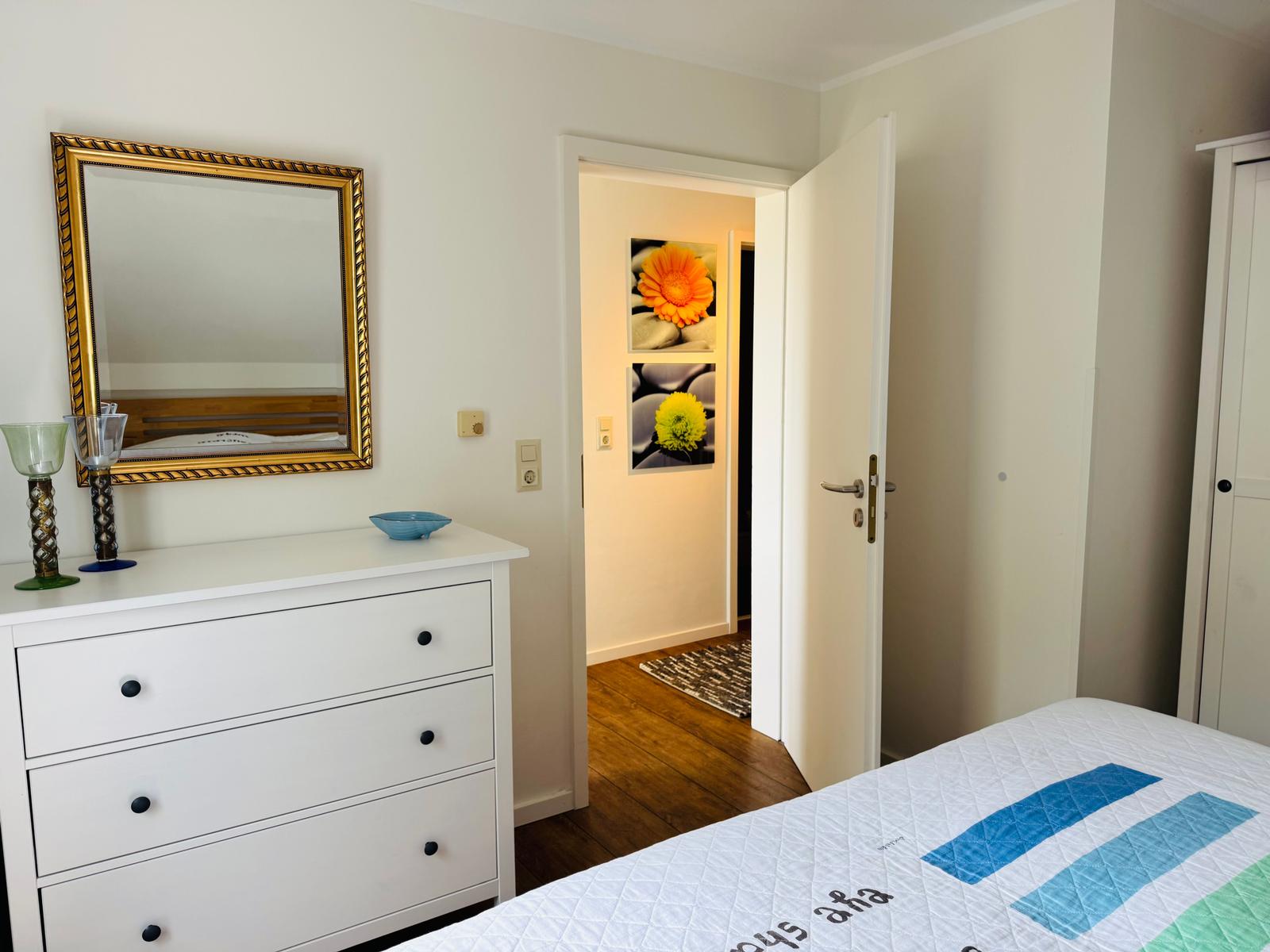 Schlafzimmer mit weißem Schrank, Spiegel und Bett mit Muster.