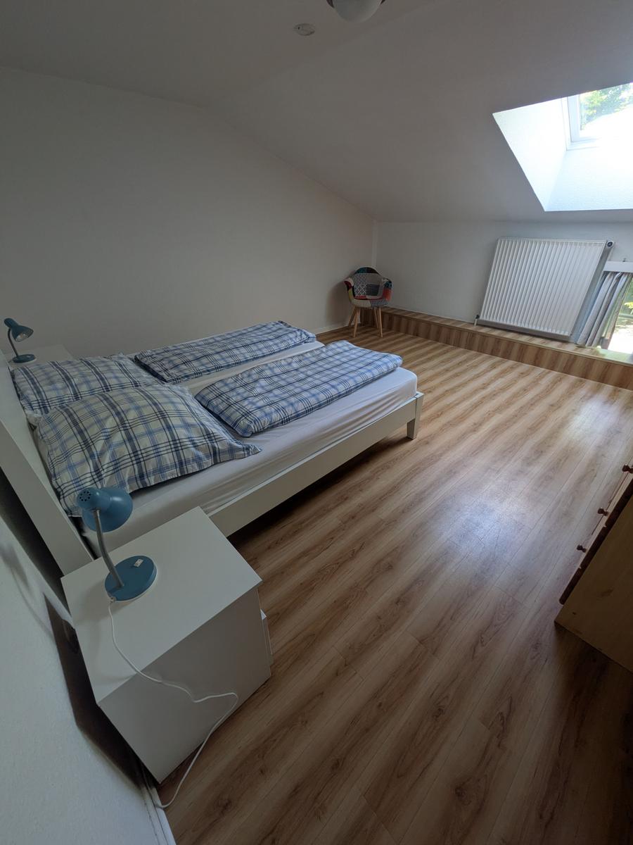 Schlafzimmer mit Dachschrägen, Dachfenster, Holzboden und Bett mit blau-weißem Bettzeug.