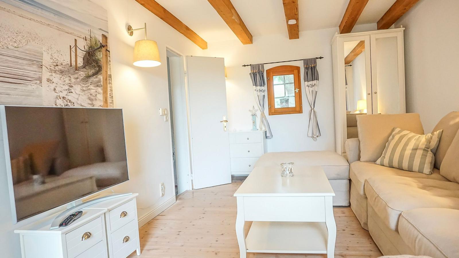 Wohnzimmer mit Sofa, Couchtisch, Fernseher und Holzbalken an der Decke.