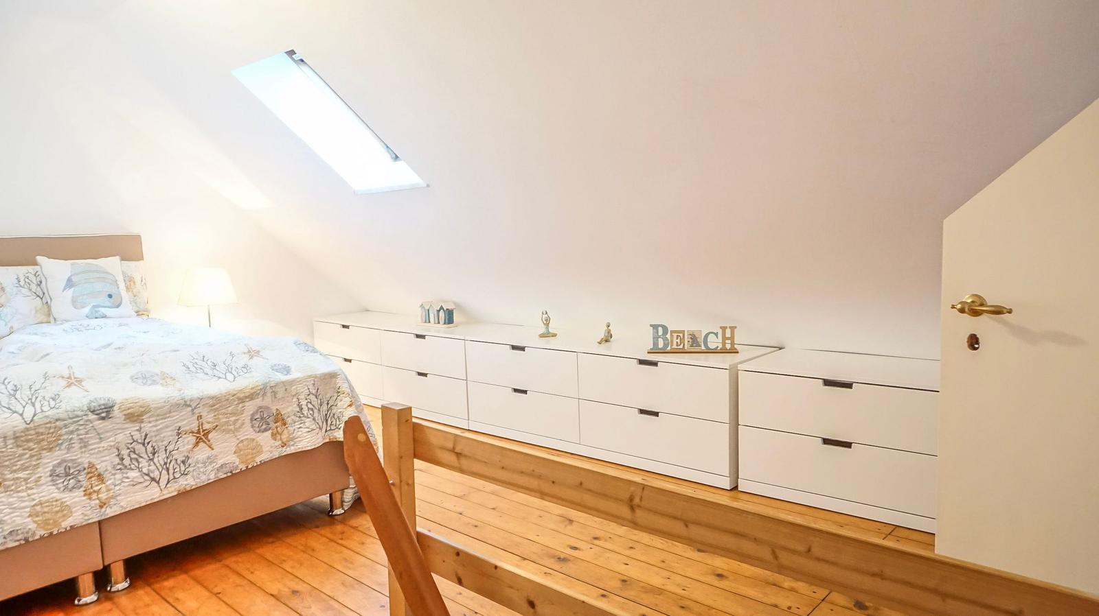 Schlafzimmer mit Dachschräge, Bett, Schrank und Dachfenster.