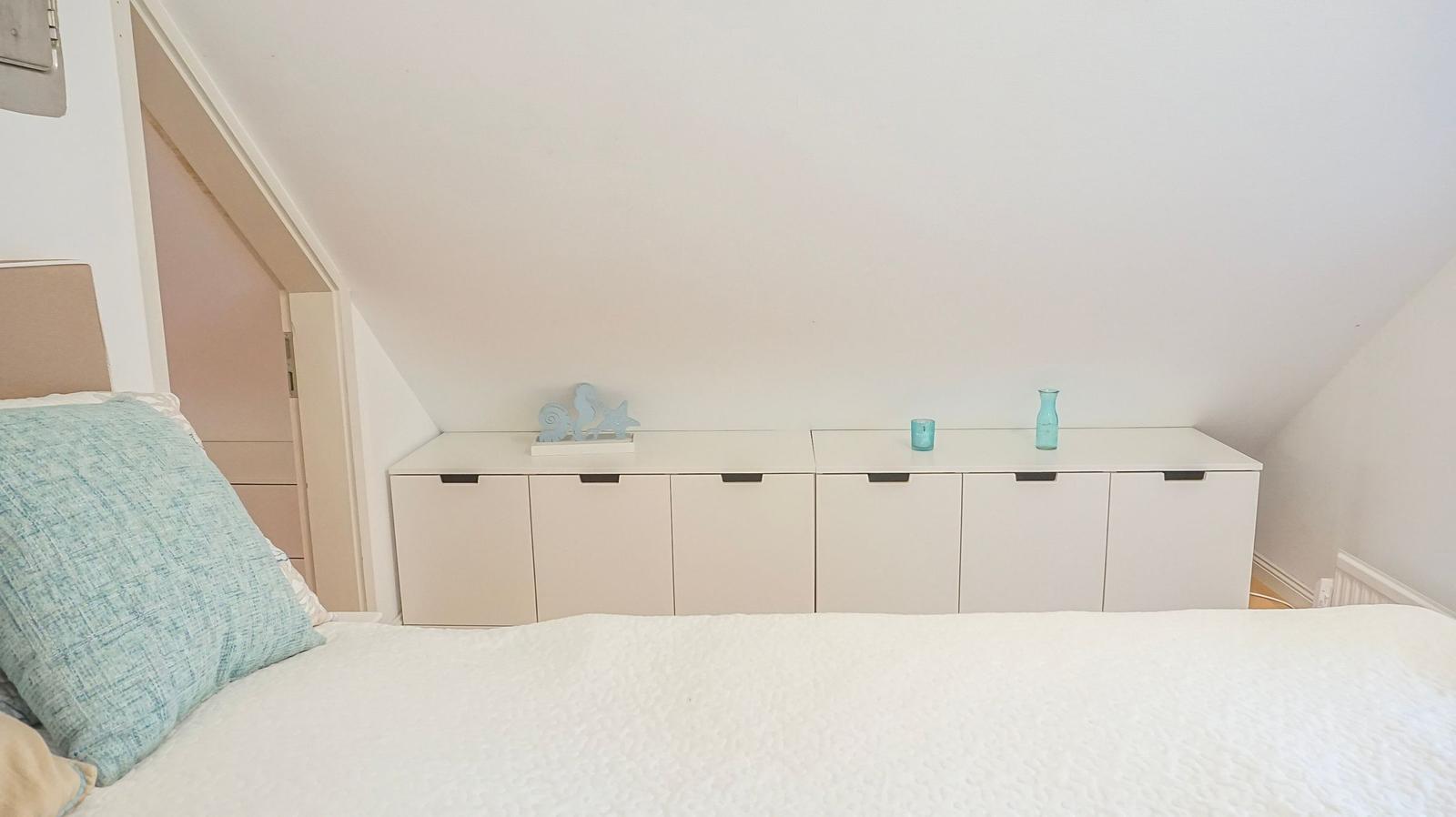 Schlafzimmer mit Dachschrägen, Bett und weißen Schränken mit Dekoration.