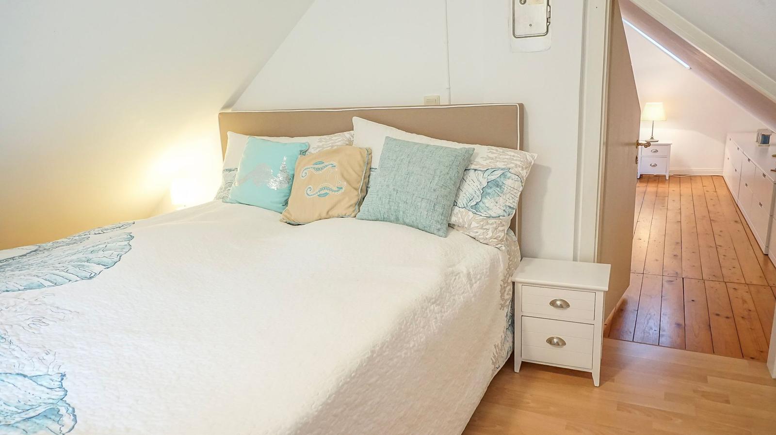 Schlafzimmer mit Bett, Kissen und Nachttisch. Holzboden und Dachschräge sichtbar.