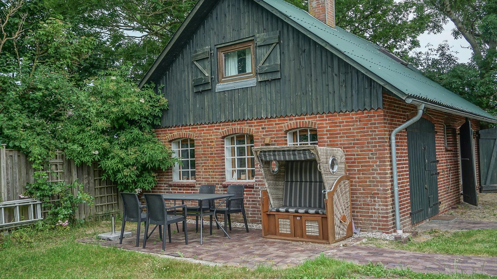 Haus mit Holz- und Ziegelbauweise, Terrasse mit Tisch, Stühlen und Liegestuhl.