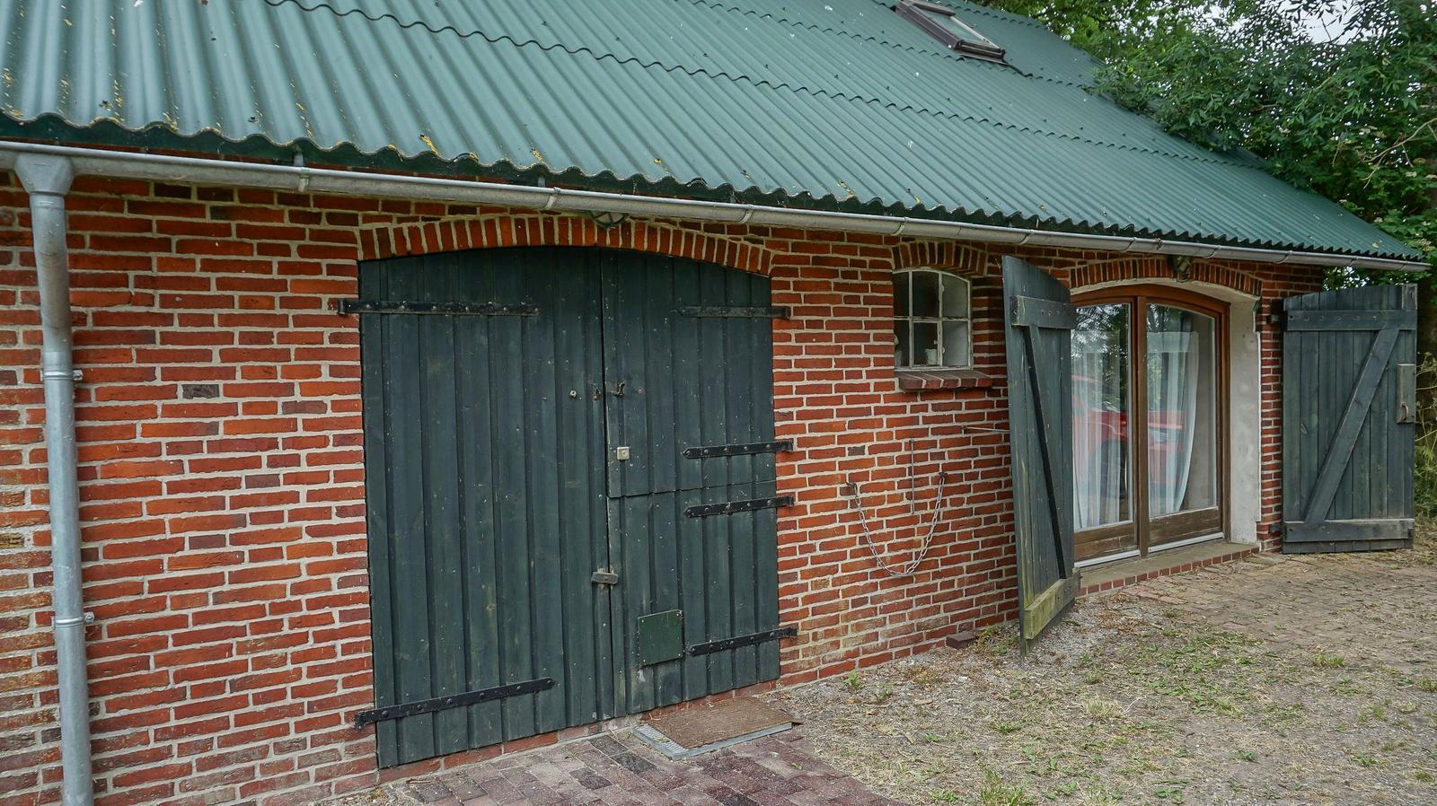 Rotes Backsteinhaus mit grünem Dach, Holztür und Fenster mit Vorhängen.