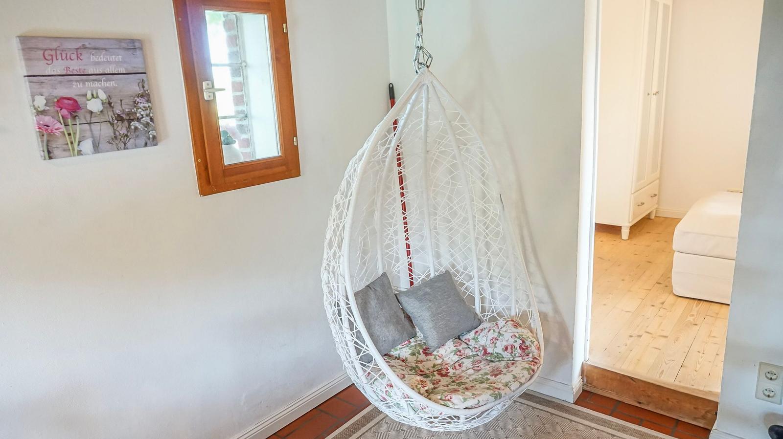 Hängesessel mit Kissen und Kissenbezug hängt in einem Raum mit Holzboden und Wandbild.