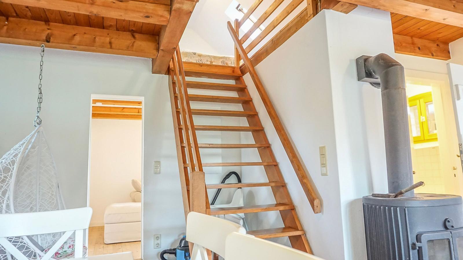 Holztreppe führt zur oberen Etage. Im Vordergrund steht ein Kaminofen.