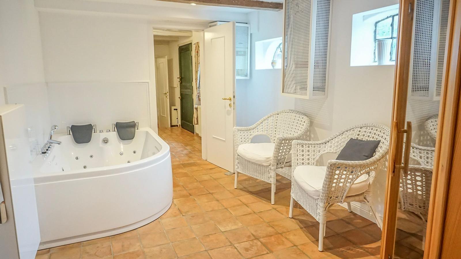 Bad mit Whirlpool, zwei weiße Rattan-Stühle und Terrakottaboden.
