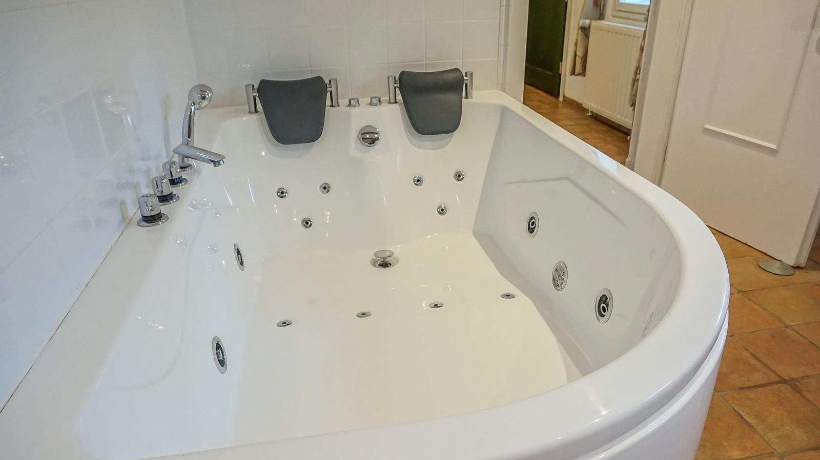 Eine große weiße Whirlpool-Badewanne mit Armlehnen und mehreren Düsen.