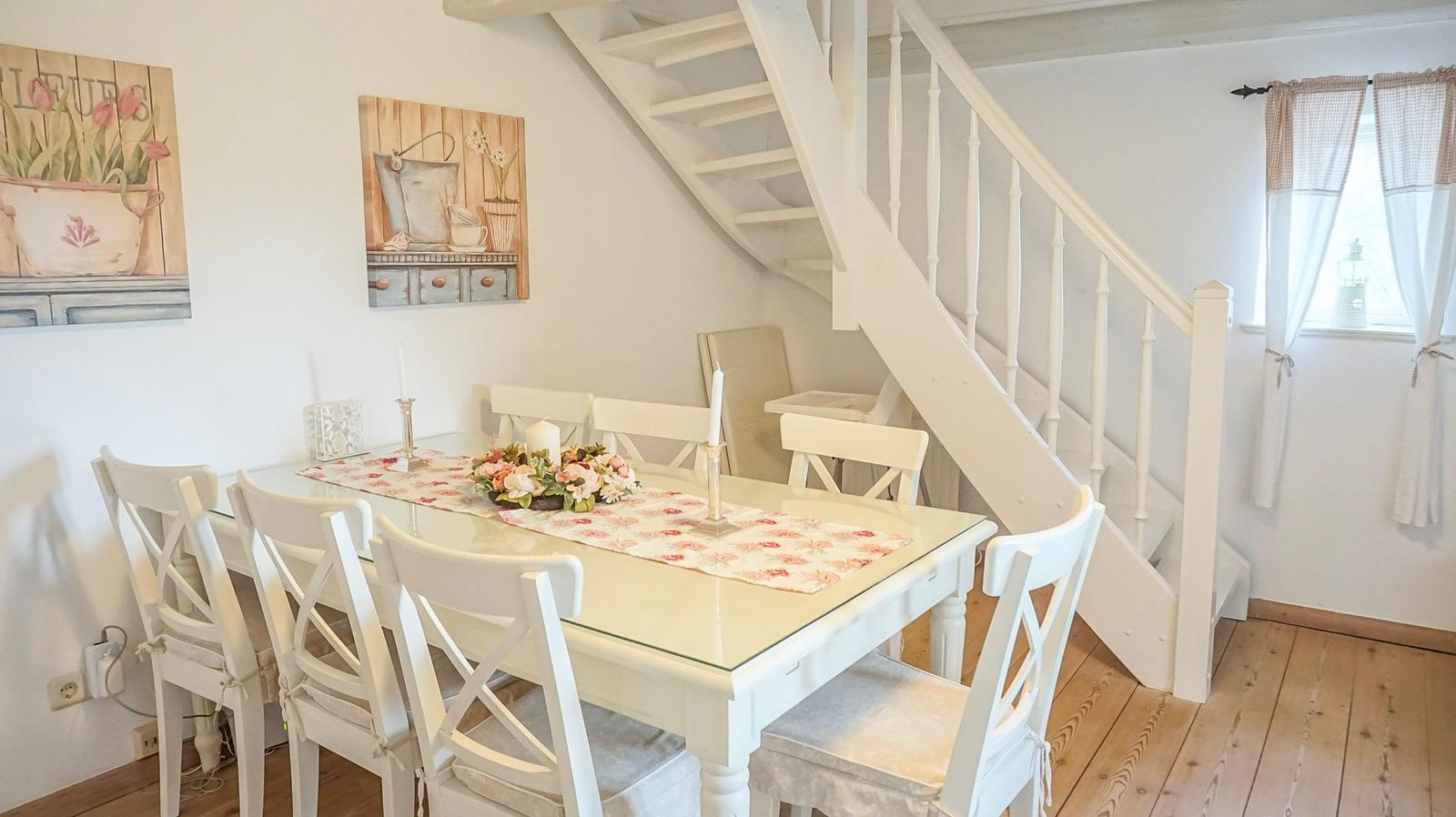 Esszimmer mit weißem Tisch, Stühlen und Tischdecke. Weiße Treppe und Holzboden.