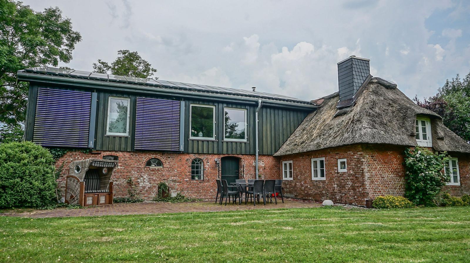 Haus mit Strohdach und Backsteinfassade, Gartenbereich mit Tisch und Stühlen.