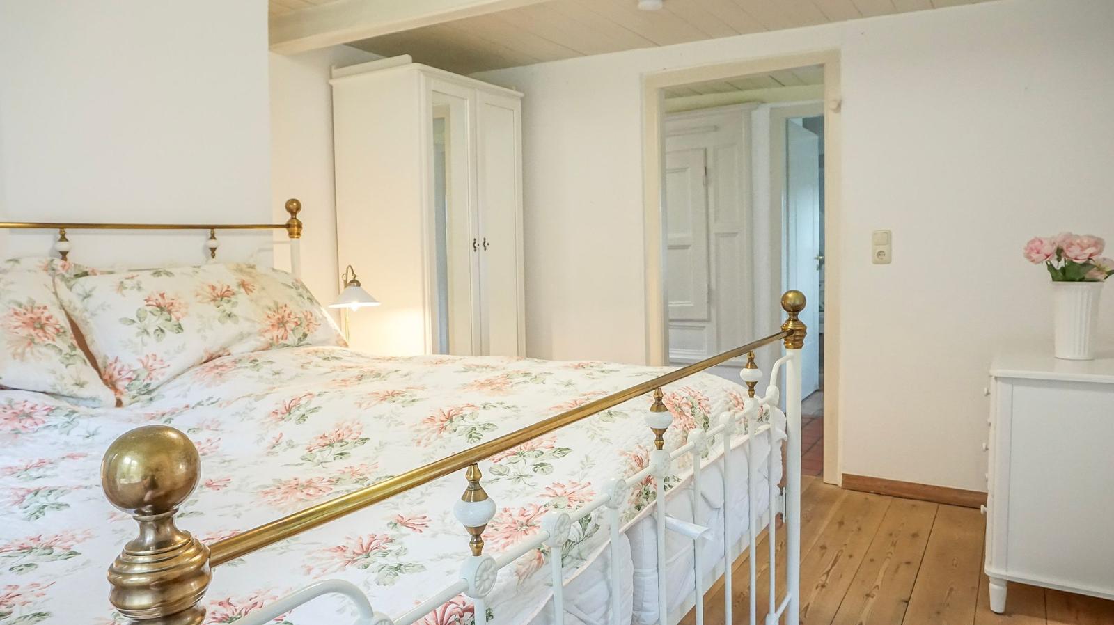 Schlafzimmer mit Bett, Kleiderschrank und Nachttisch. Holzboden und weiße Wände.