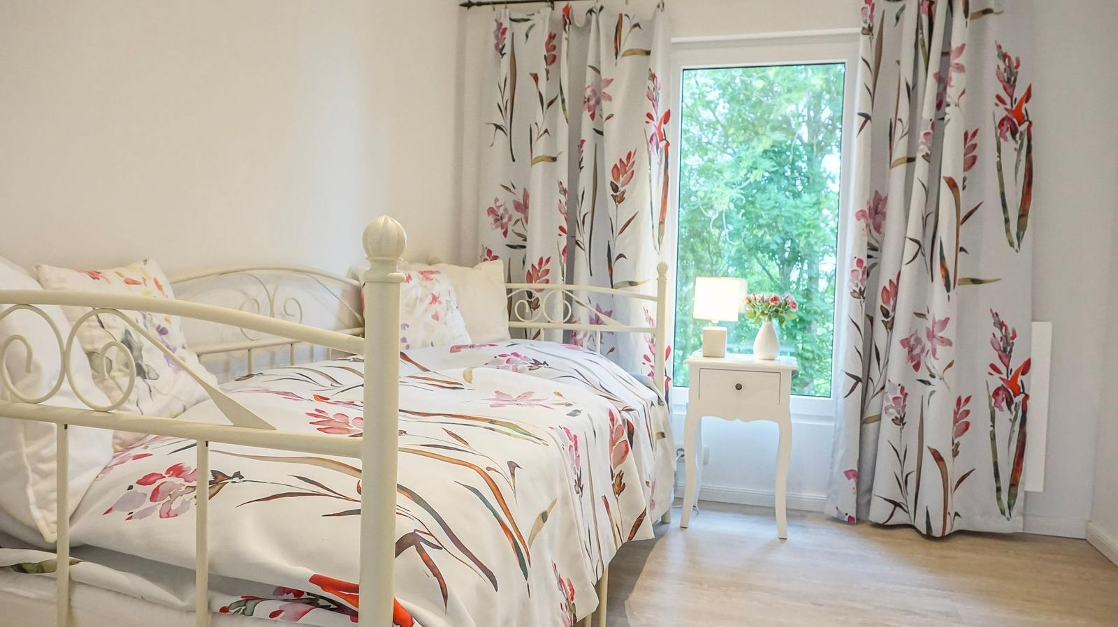 Schlafzimmer mit Bett, Vorhängen und Nachttisch vor Fenster