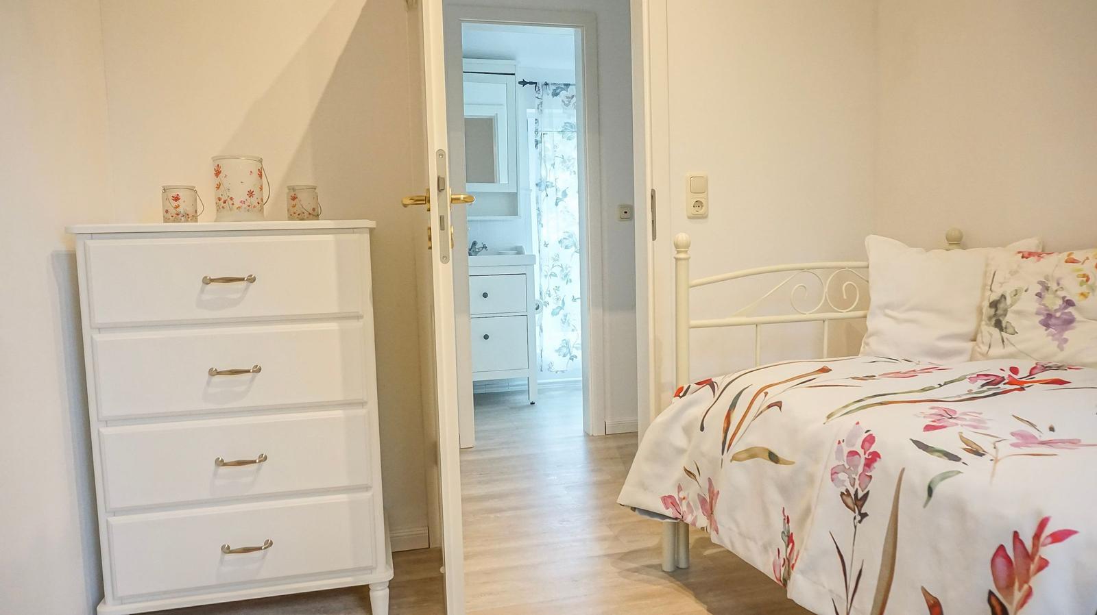 Schlafzimmer mit Bett und Schrank. Durchgang zur Badewanne.