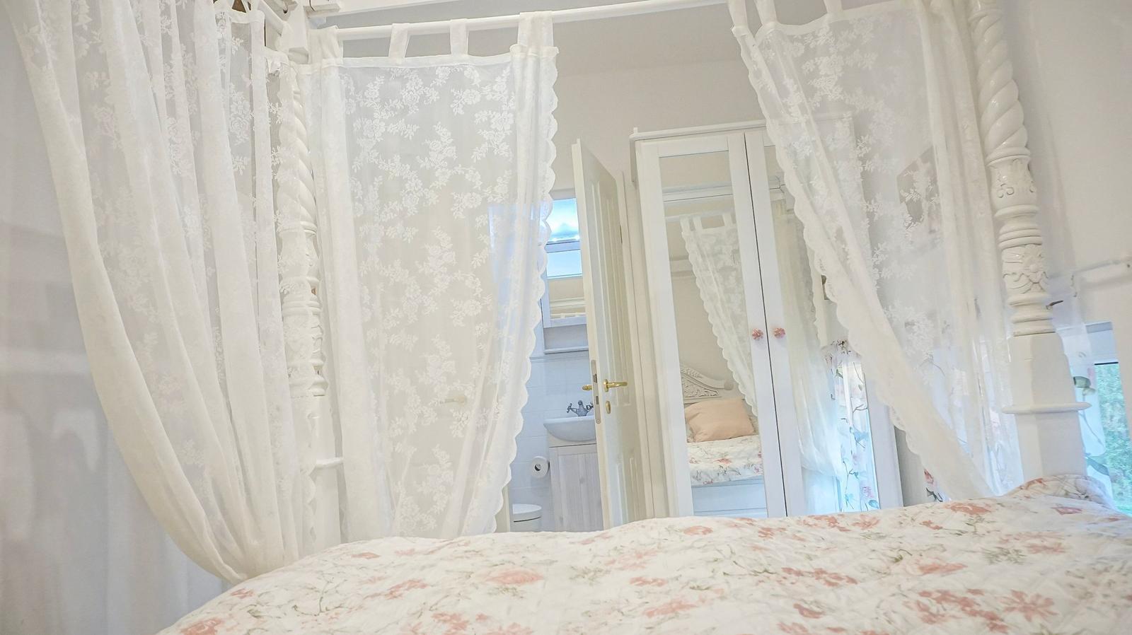 Schlafzimmer mit weißem Baldachin, floraler Bettdecke und Blick in Badezimmer.