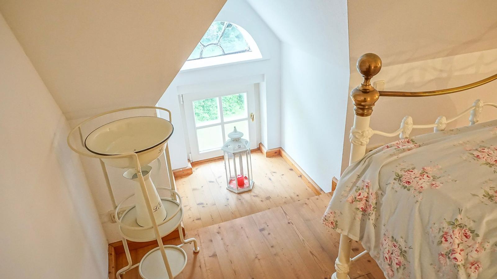 Schlafzimmer mit Bett, Holzboden und Fenster. Weiße Wand und goldener Bettkopf.