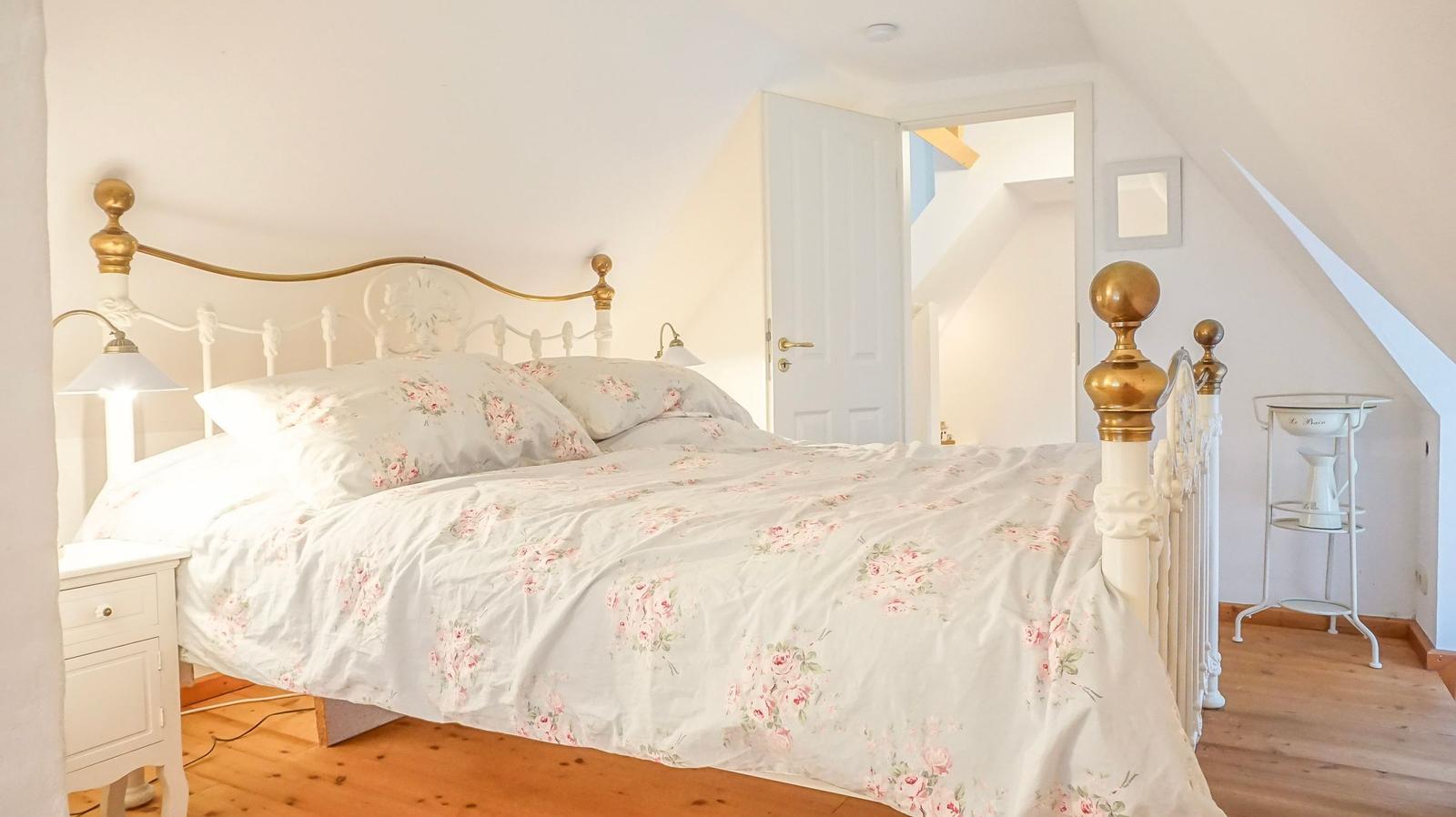 Schlafzimmer mit Bett, Nachttisch und Tür. Holzboden und schräger Dachfirst.