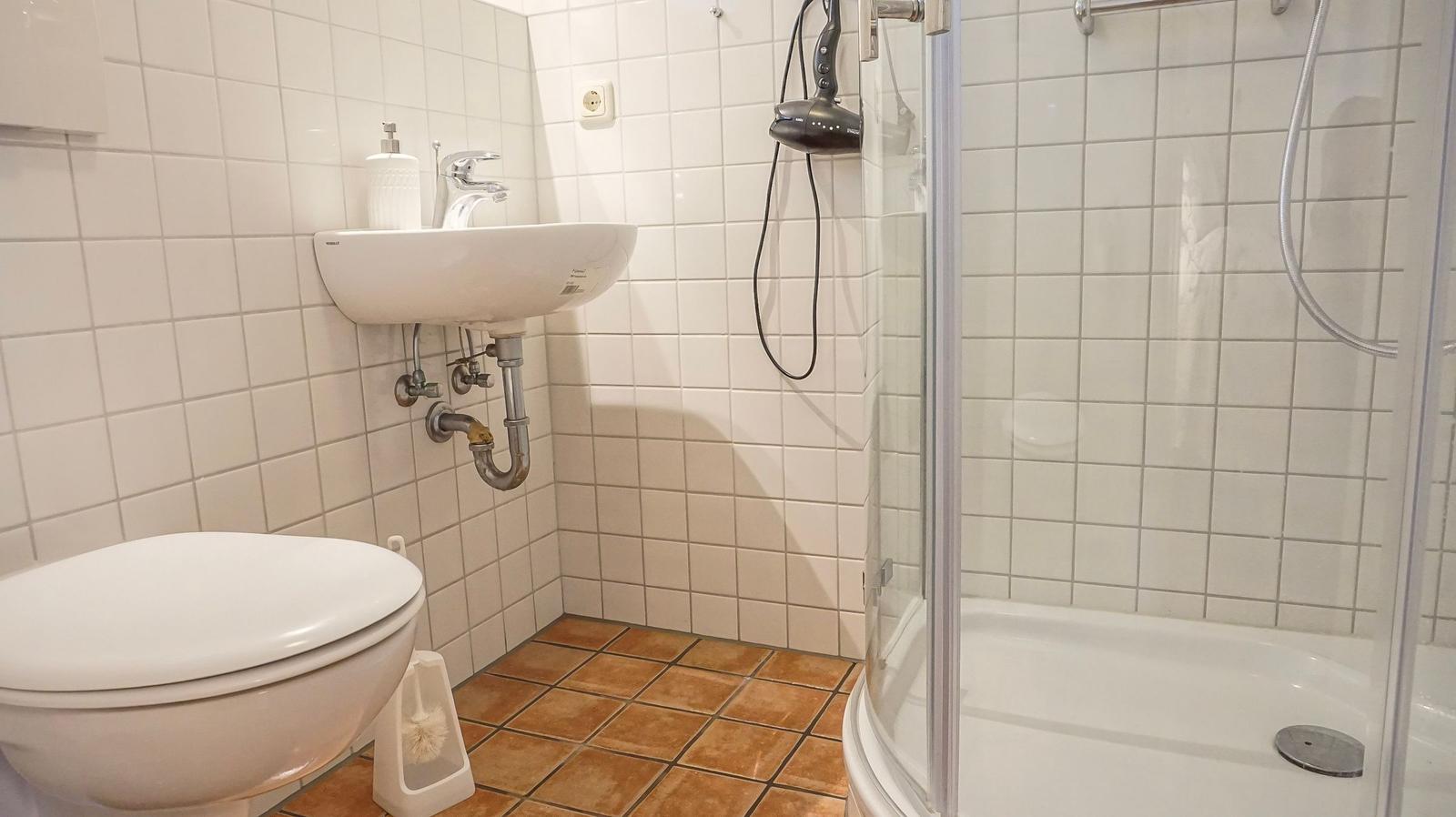 Badezimmer mit Toilette, Waschbecken und Dusche mit Glaswand.