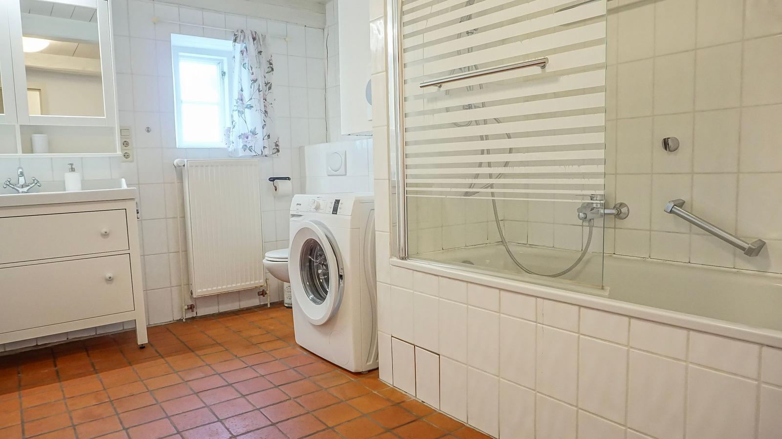 Badezimmer mit Badewanne, Dusche, Waschmaschine und Waschtisch.