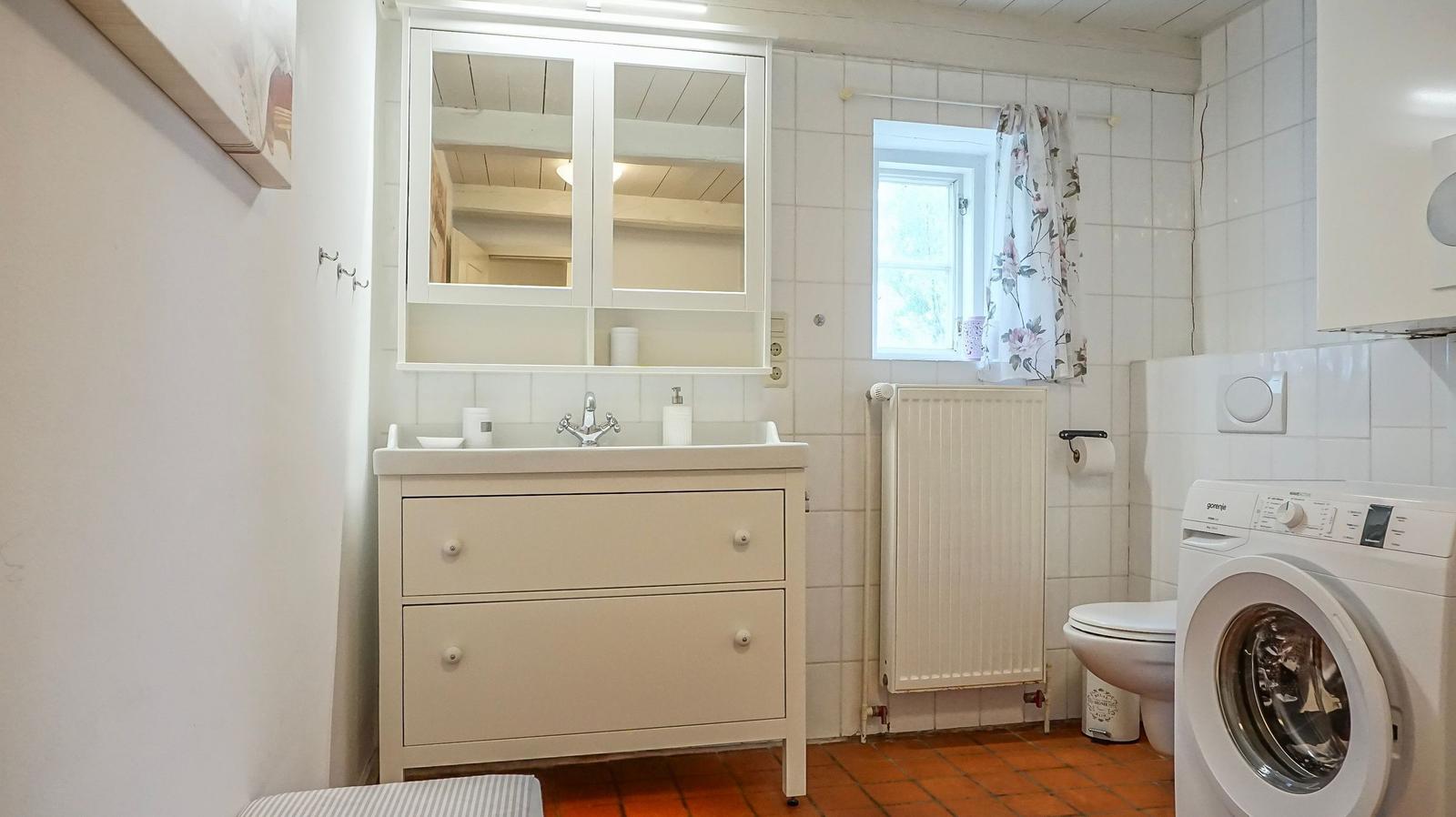 Badezimmer mit Waschmaschine, Toilette und Spiegelschrank.