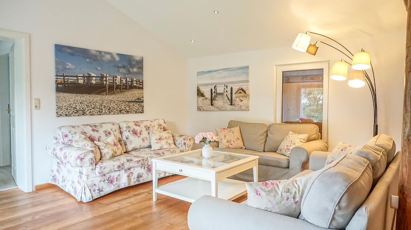 Wohnzimmer mit drei Sofas, Glas-Tisch und Wandbildern an den Wänden.