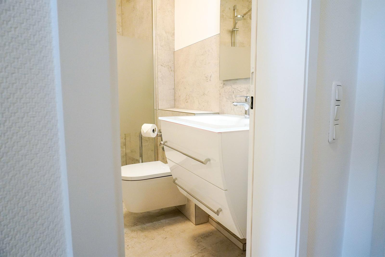 Badezimmer mit Waschbecken, Toilette und Dusche. Fliesen und weiße Einrichtung.