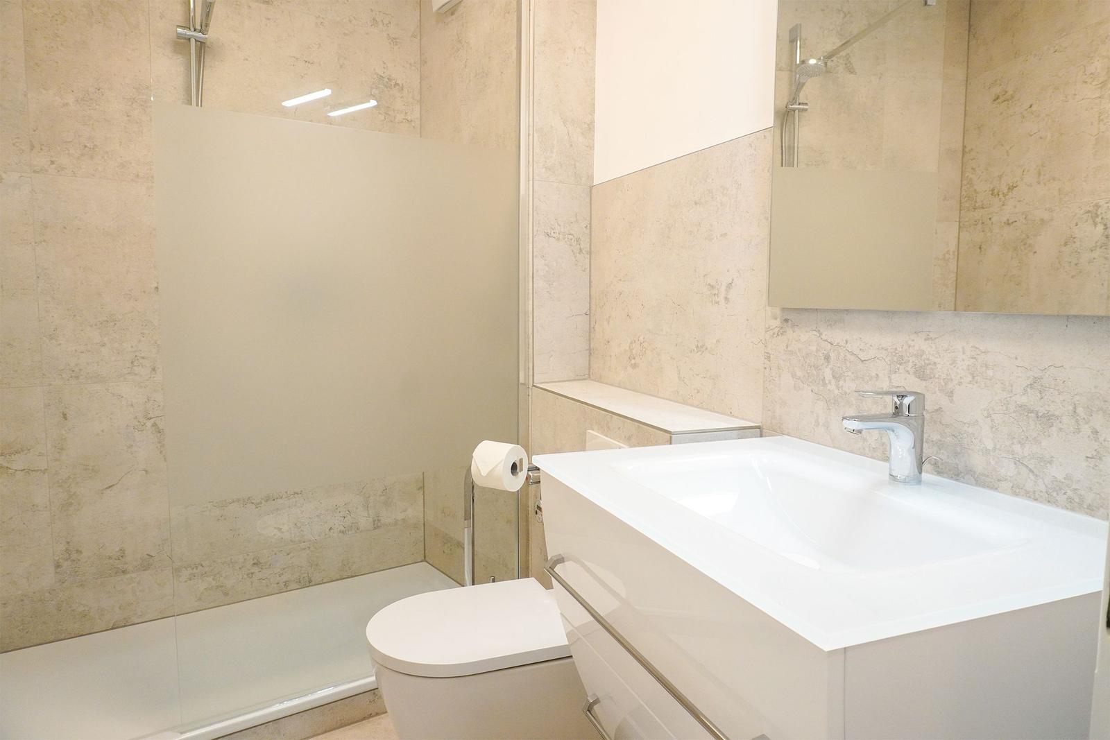 Bad mit Dusche, Waschbecken und Toilette. Fliesenwand und Spiegel.
