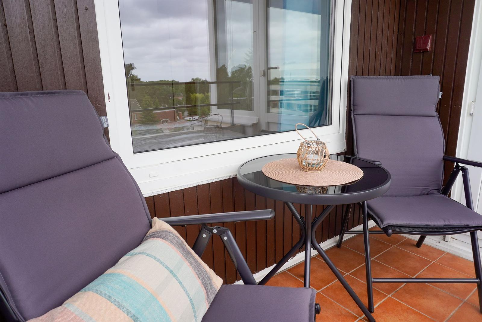 Terrasse mit zwei Stühlen, Tisch und dekorativer Laterne. Holzwand und Fenster im Hintergrund.