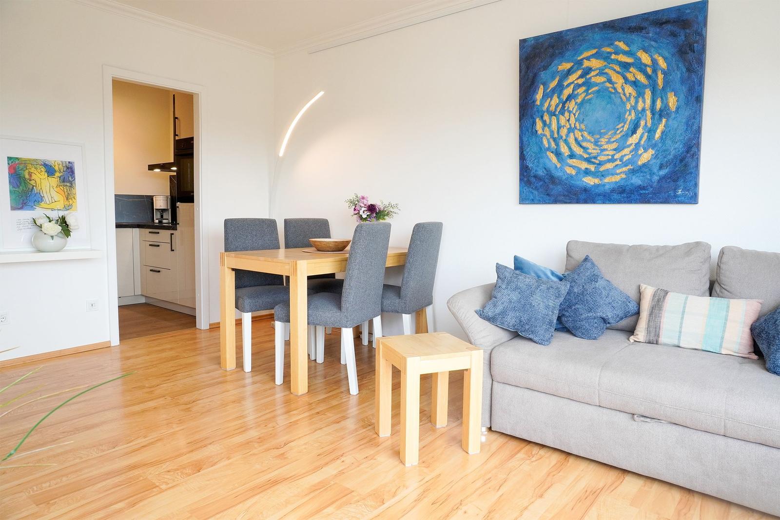 Wohn- und Essbereich mit Sofa, Tisch und Stühlen. Holzboden und Wandkunst sichtbar.