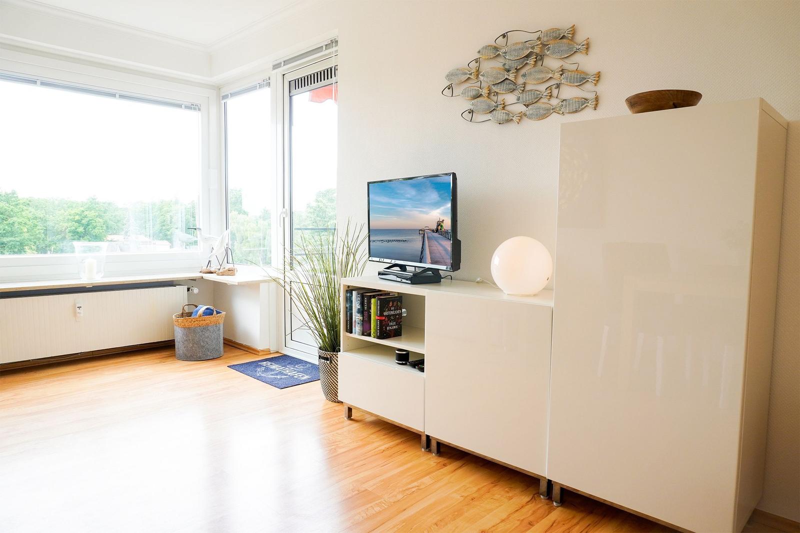 Wohnzimmer mit TV, Schrank und Fensterblick auf Grünflächen.
