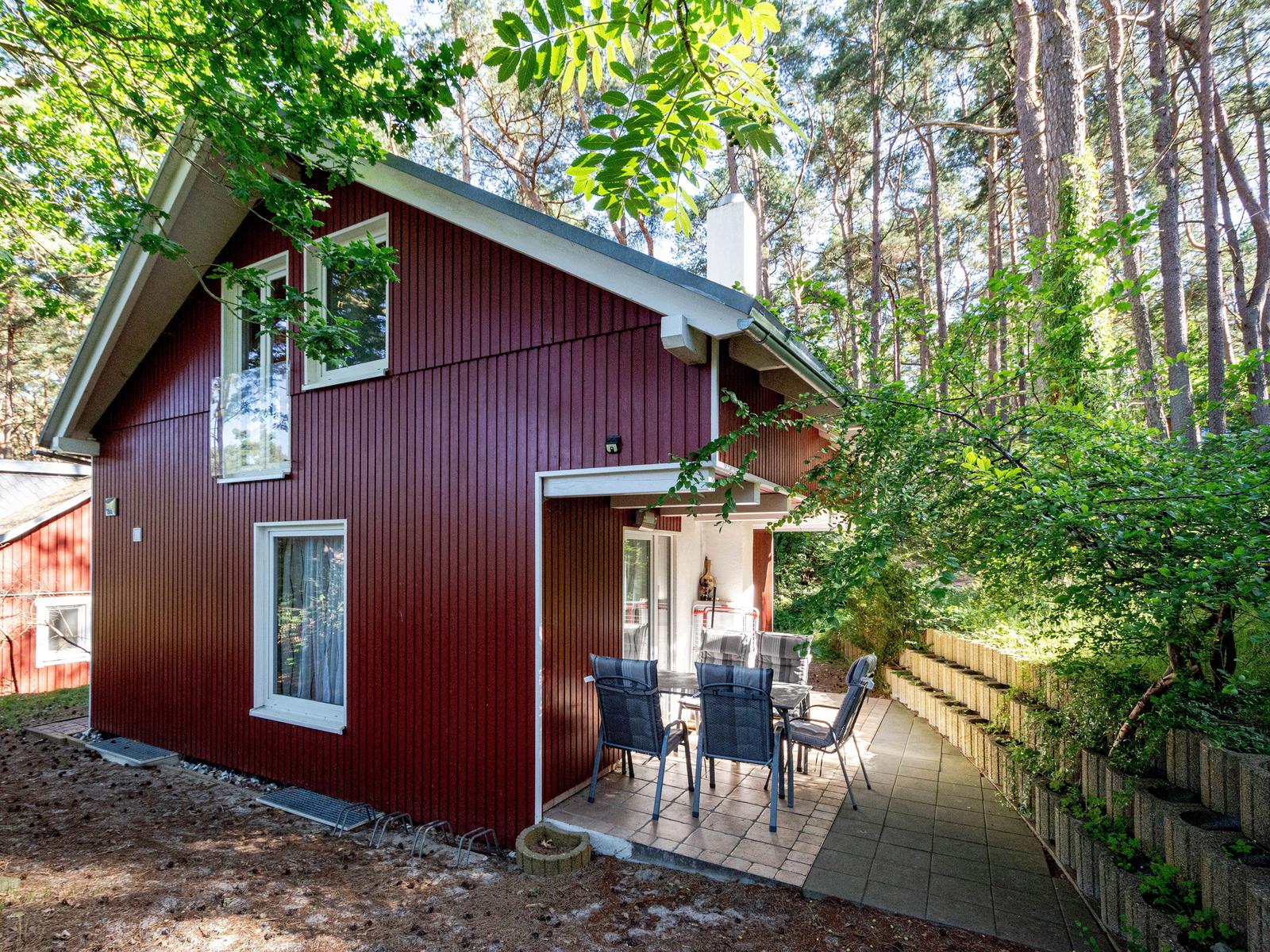 Rotes Holzhaus mit Terrasse und Garten in Waldnähe.