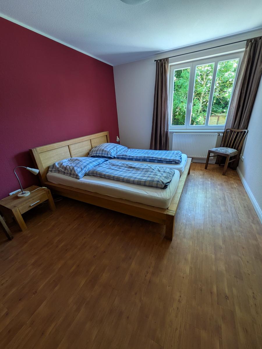 Schlafzimmer mit Doppelbett, Holzboden und Fenster mit Blick auf Grün.