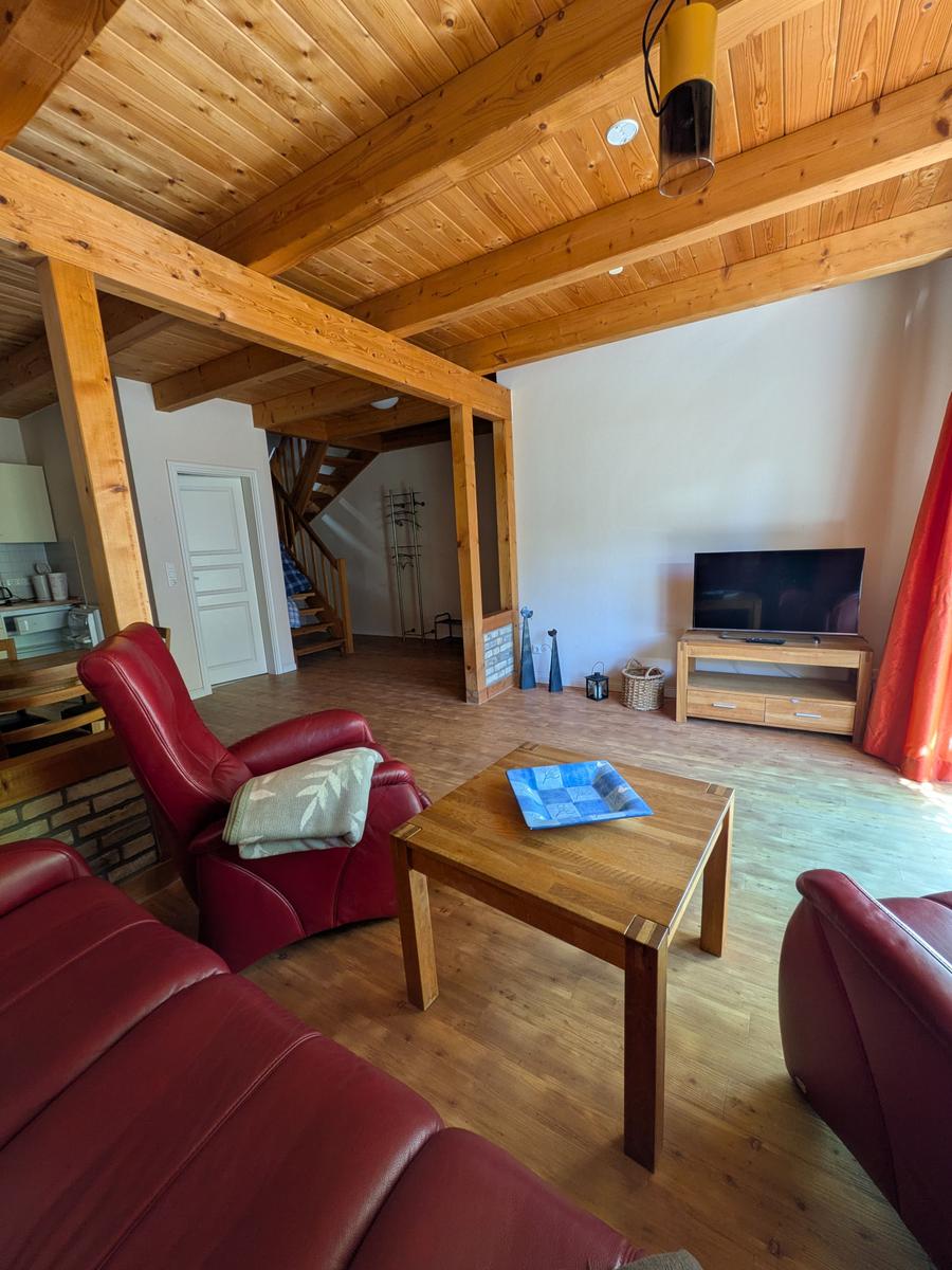 Wohnzimmer mit rotem Ledersofa, Holztisch und Fernseher. Holzdecke und Boden.