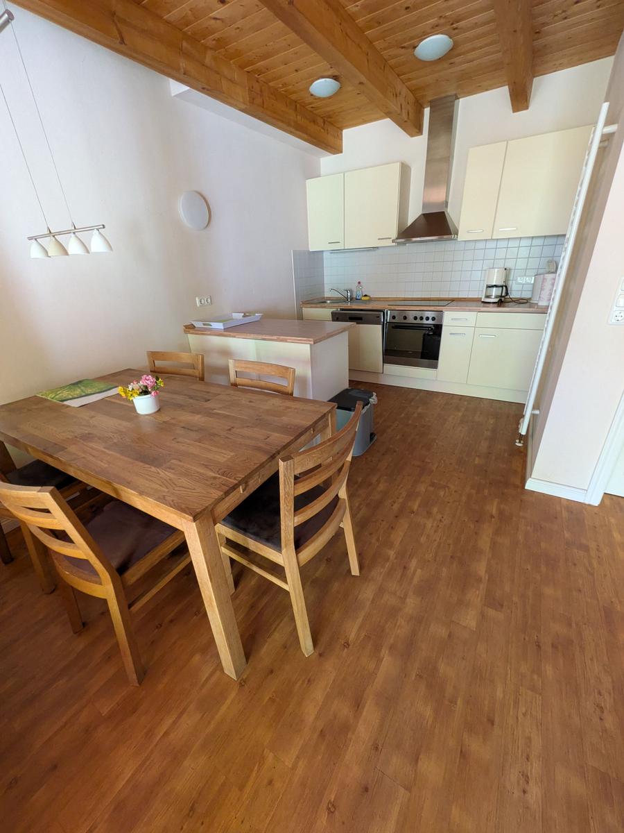 Essbereich mit Holztisch und Stühlen, Küche mit Küchenzeile und Holzboden.