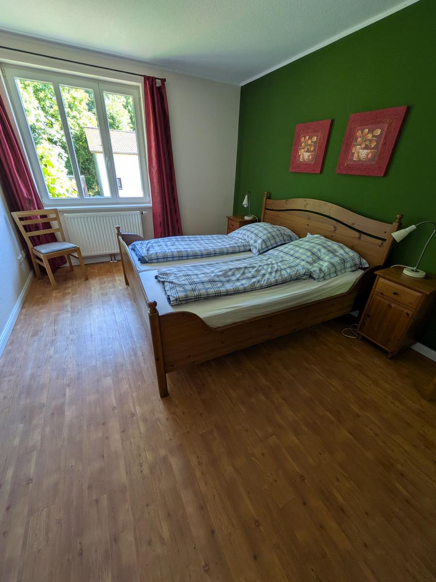 Schlafzimmer mit Holzbett, grüner Wand und Fenster mit roten Vorhängen.