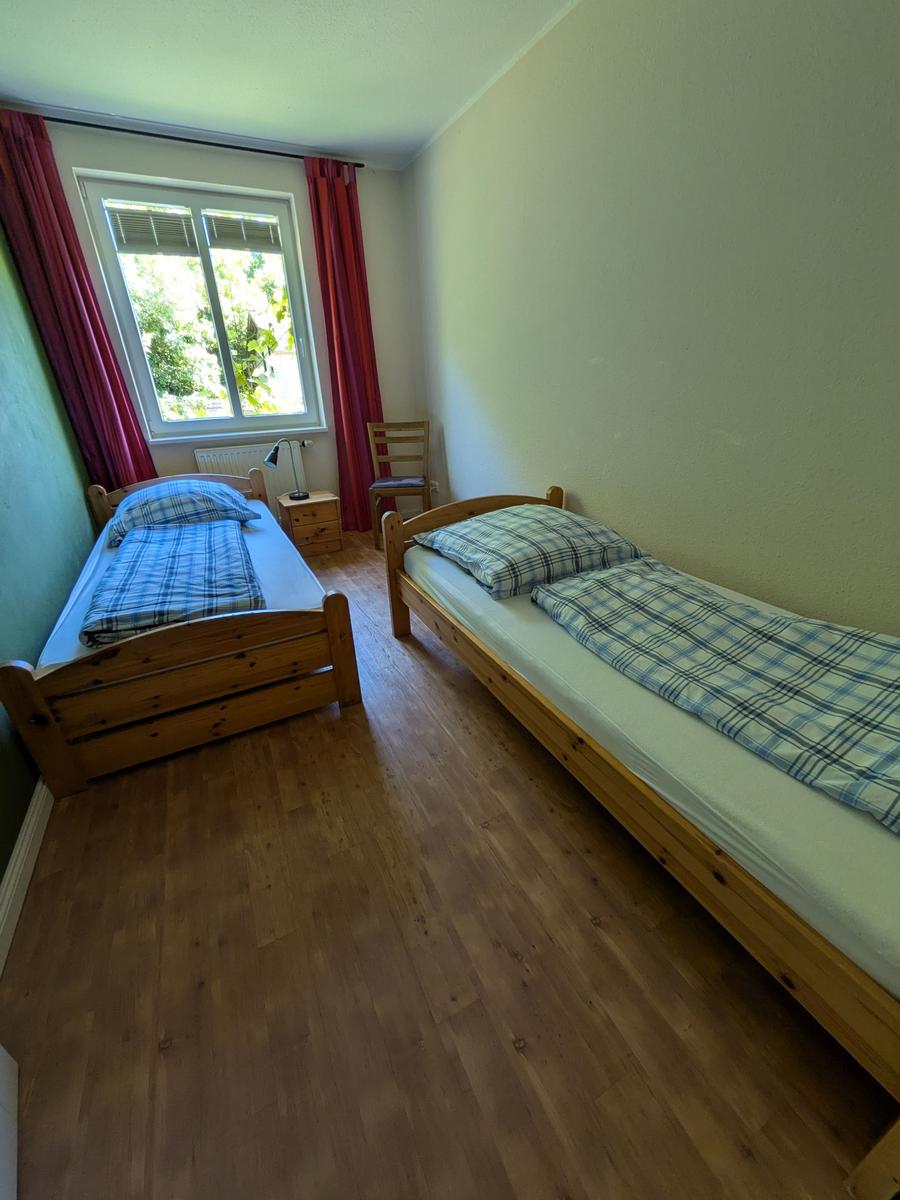 Zwei Einzelbetten, Holzboden, Fenster mit roten Vorhängen und Stuhl.