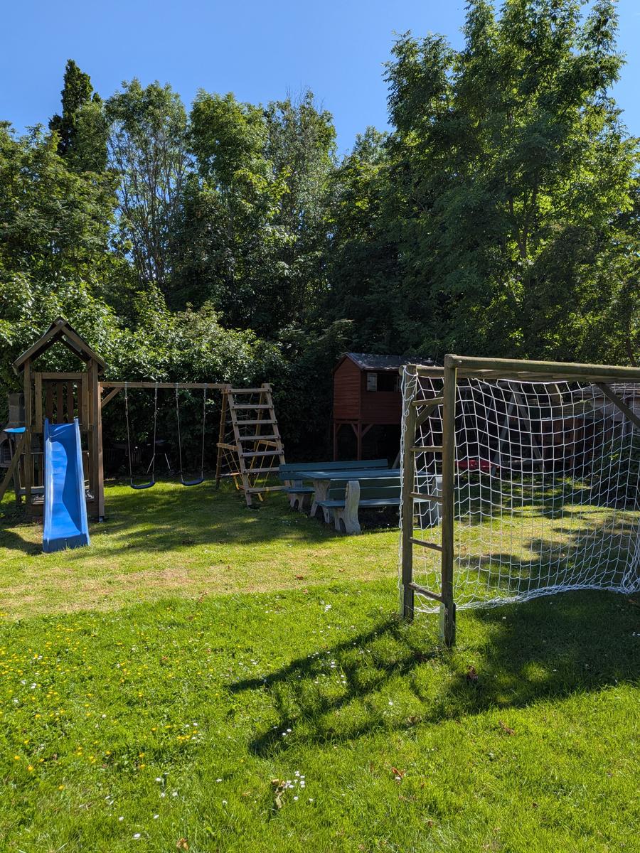 Hinterhof mit Spielplatz, Fußballtor und Picknicktisch unter Bäumen.