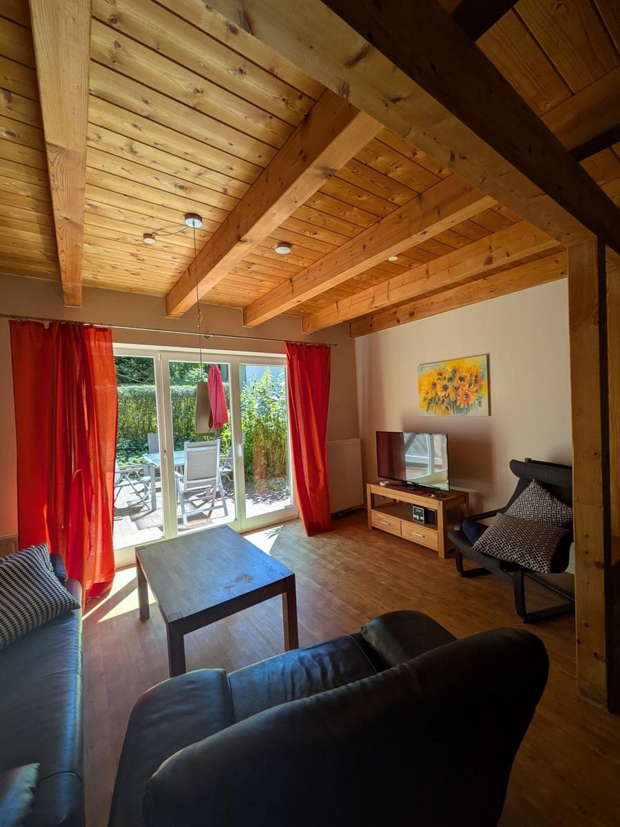 Wohnzimmer mit Holzdecke, roten Vorhängen und Blick auf die Terrasse.