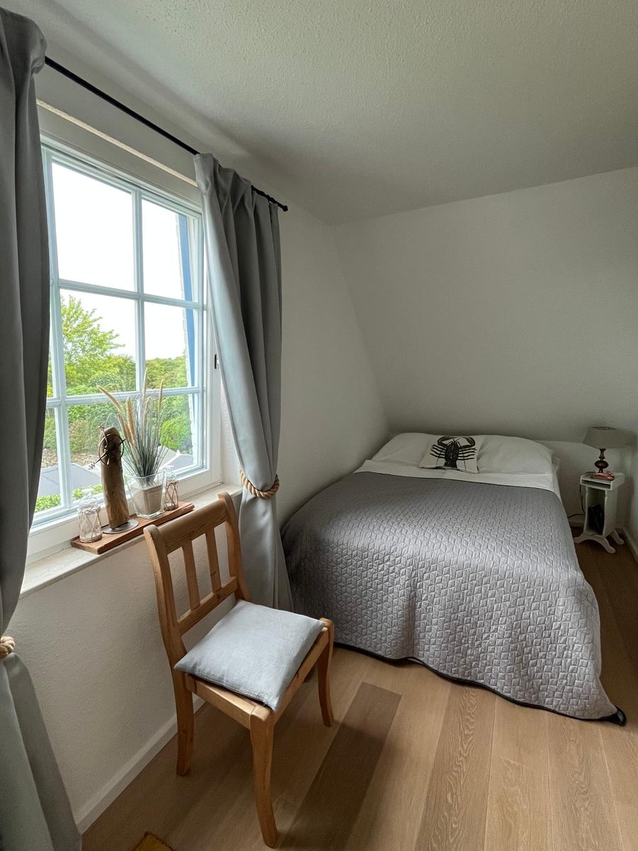 Schlafzimmer mit Bett, Stuhl und Fenster mit Blick auf Grün.