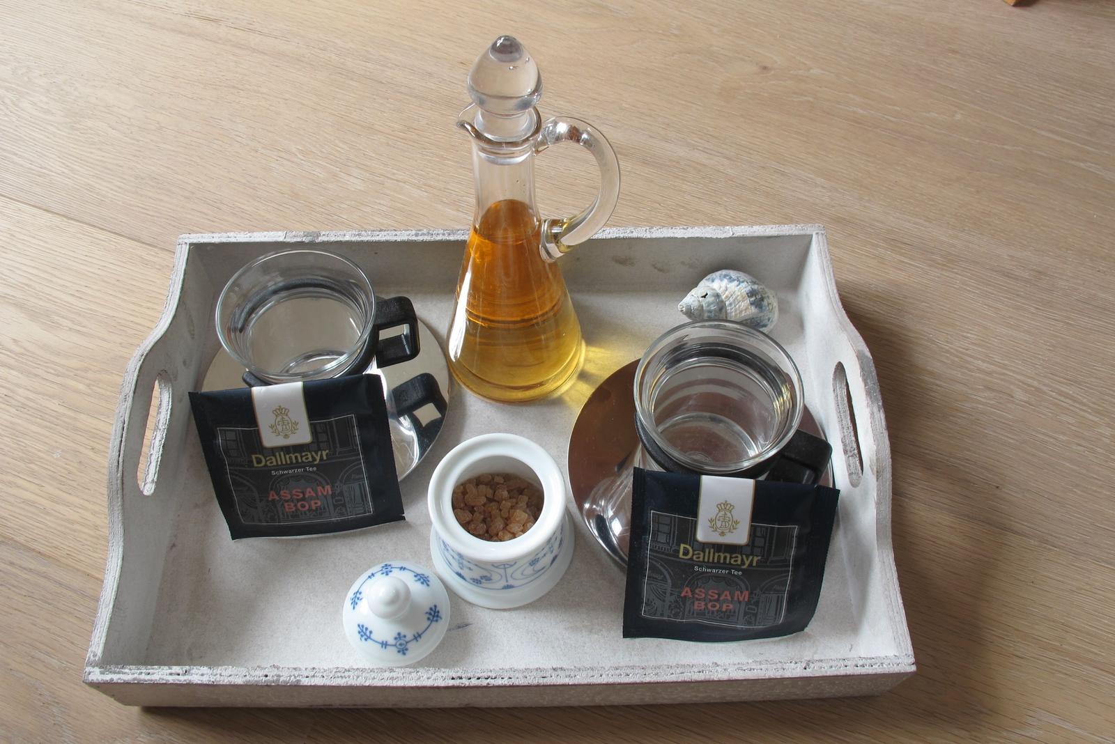 Teetisch mit zwei Tassen, Zuckerdose, Ölflasche und Teepackungen auf Holztablett.