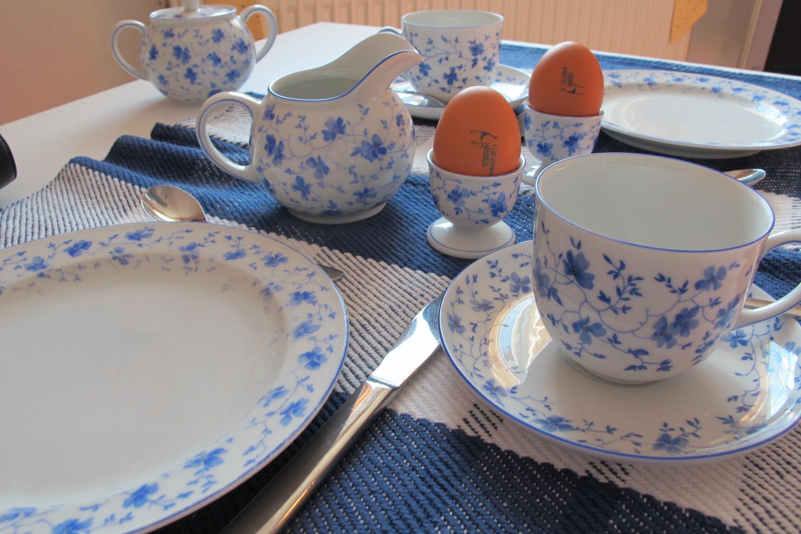 Tisch gedeckt mit blau-weißem Geschirr, zwei Eier in Eierbechern und Besteck.