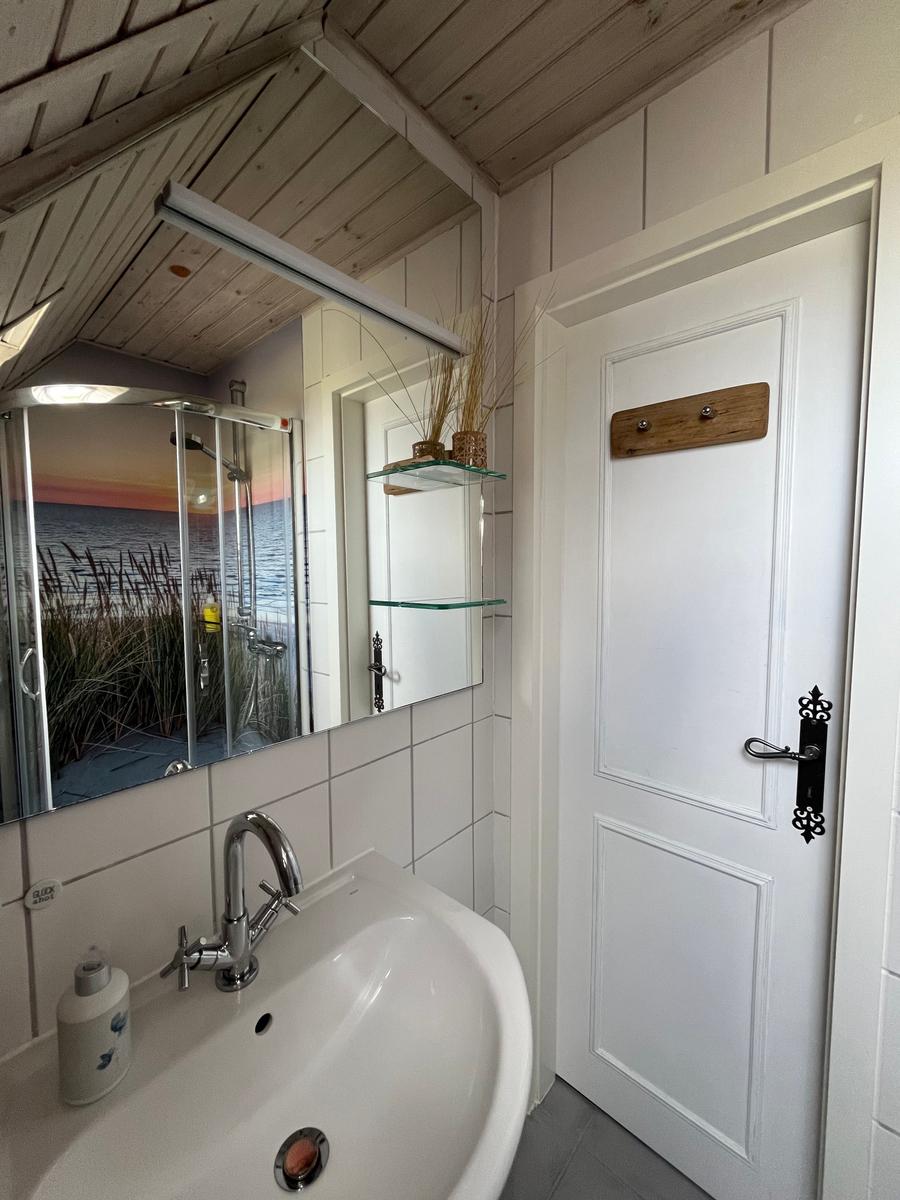Bad mit Waschbecken, Spiegel und Dusche mit Meeresbild.